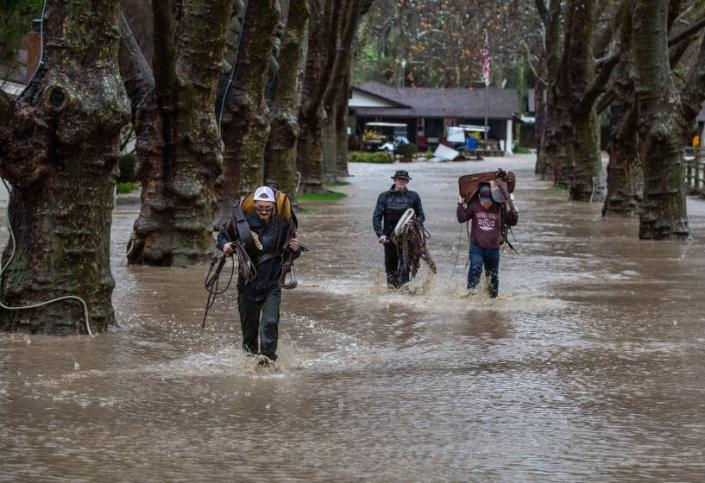 Men carry horse tack down a flooded road at Alisal Guest Ranch & Resort in Solvang on Monday. (George Rose / Getty Images)